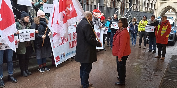 Lars Hartwig spricht mit Ute Reimers-Bruns; im Hintergrund Teilnehmer:innen der Protestaktion mit Fahnen und Transparenten