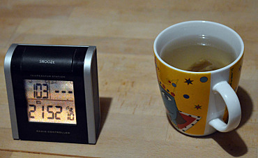 Ein Becher mit Tee auf einem Tisch. Daneben steht eine Uhr mit Temperaturanzeige. Sie zeigt 21:52 Uhr und 10,3 Grad